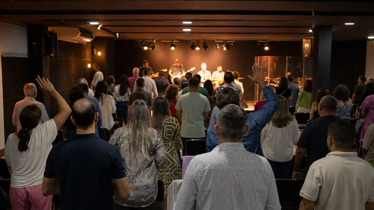 Interior de uma igreja simples durante o culto de domingo à noite, com pessoas de pé cantando, vistas de costas